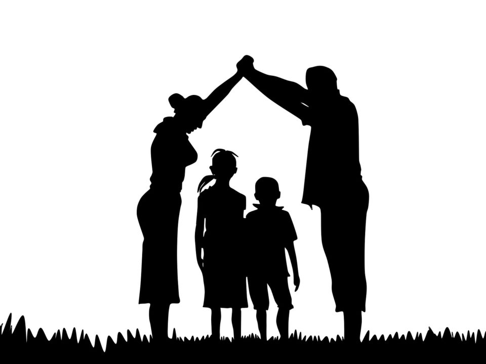Silhouette einer Familie. Mann und Frau bilden mit ihren Armen ein Dach über zwei Kindern.