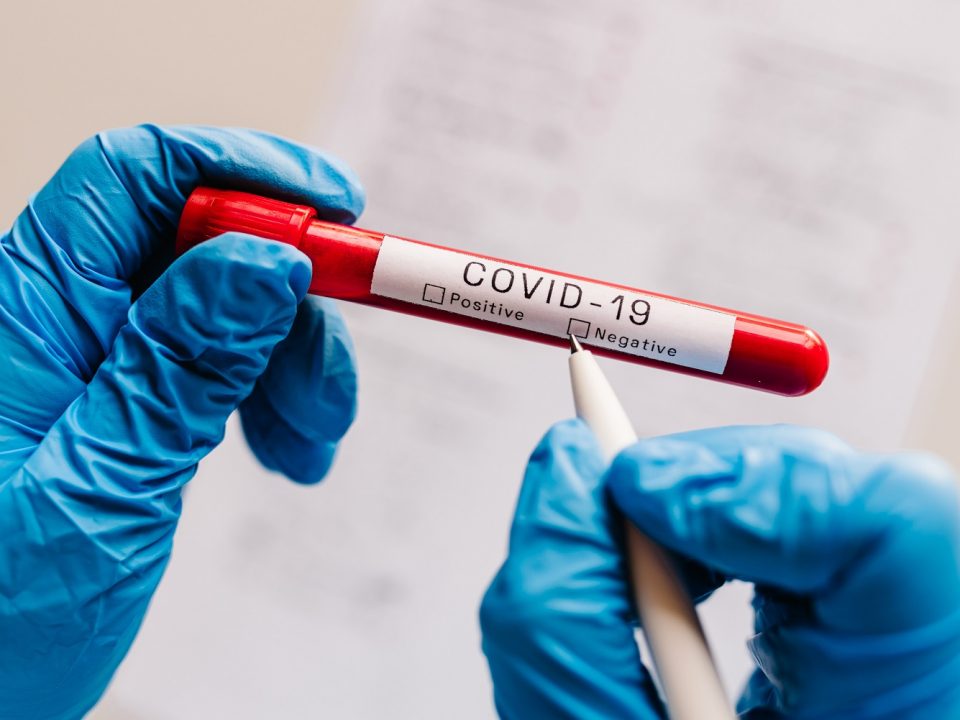 Zwei Hände in blauen Handschuhen halten ein Coronavirus-Teströhrchen in den Händen.
