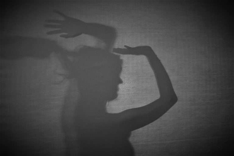 Silhouette: Einer Frau wird von hinten an den Haaren gezogen. Sie hebt die Hände.