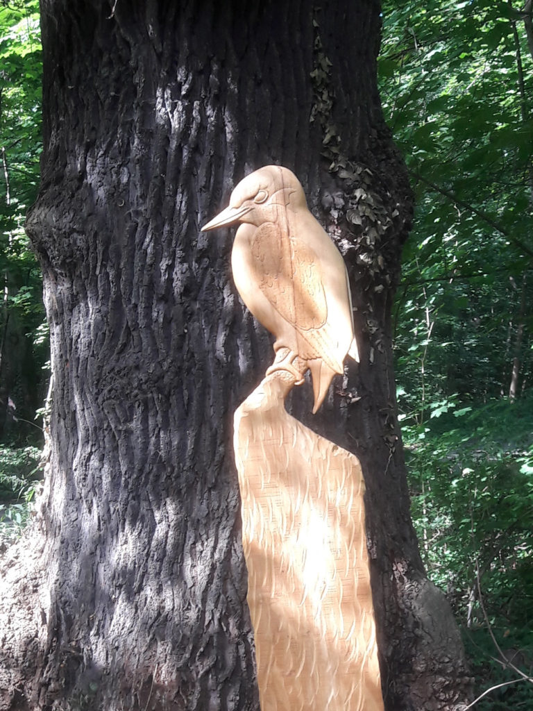 Ein aus Holz geschnitzter Eisvogel auf einer Holzstele im Wald.