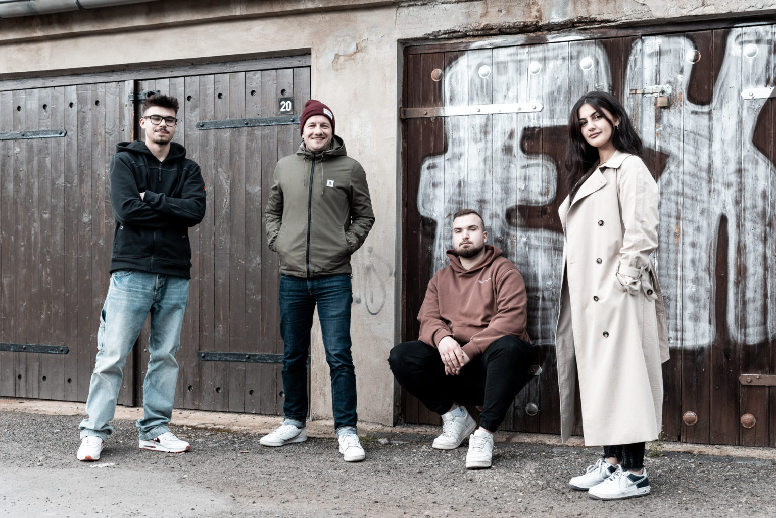 Drei junge Menschen stehen und eine Person hockt vor einem Garagentor.