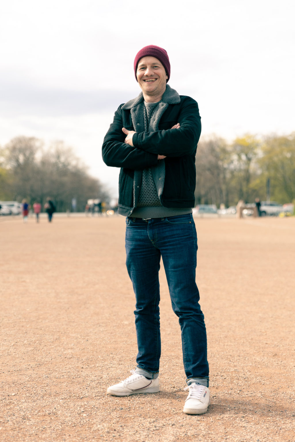 Ein Mann steht mit verschränkten Armen auf einer roten, sandigen Fläche.