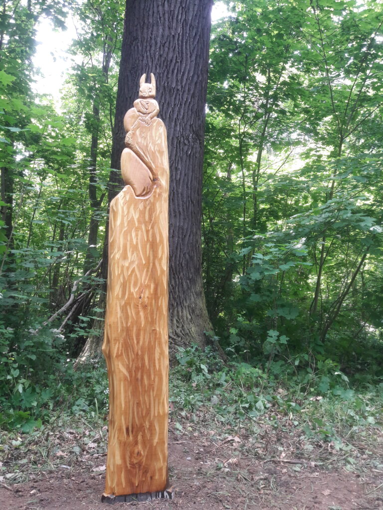 Eine Holzstele mit eingearbeitetem Eichhörnchen steht im Wald.