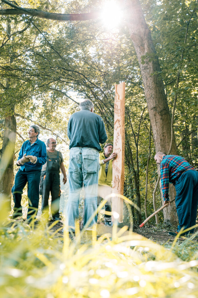 Mehrere Männer stellen eine Holzstele im Wald auf.