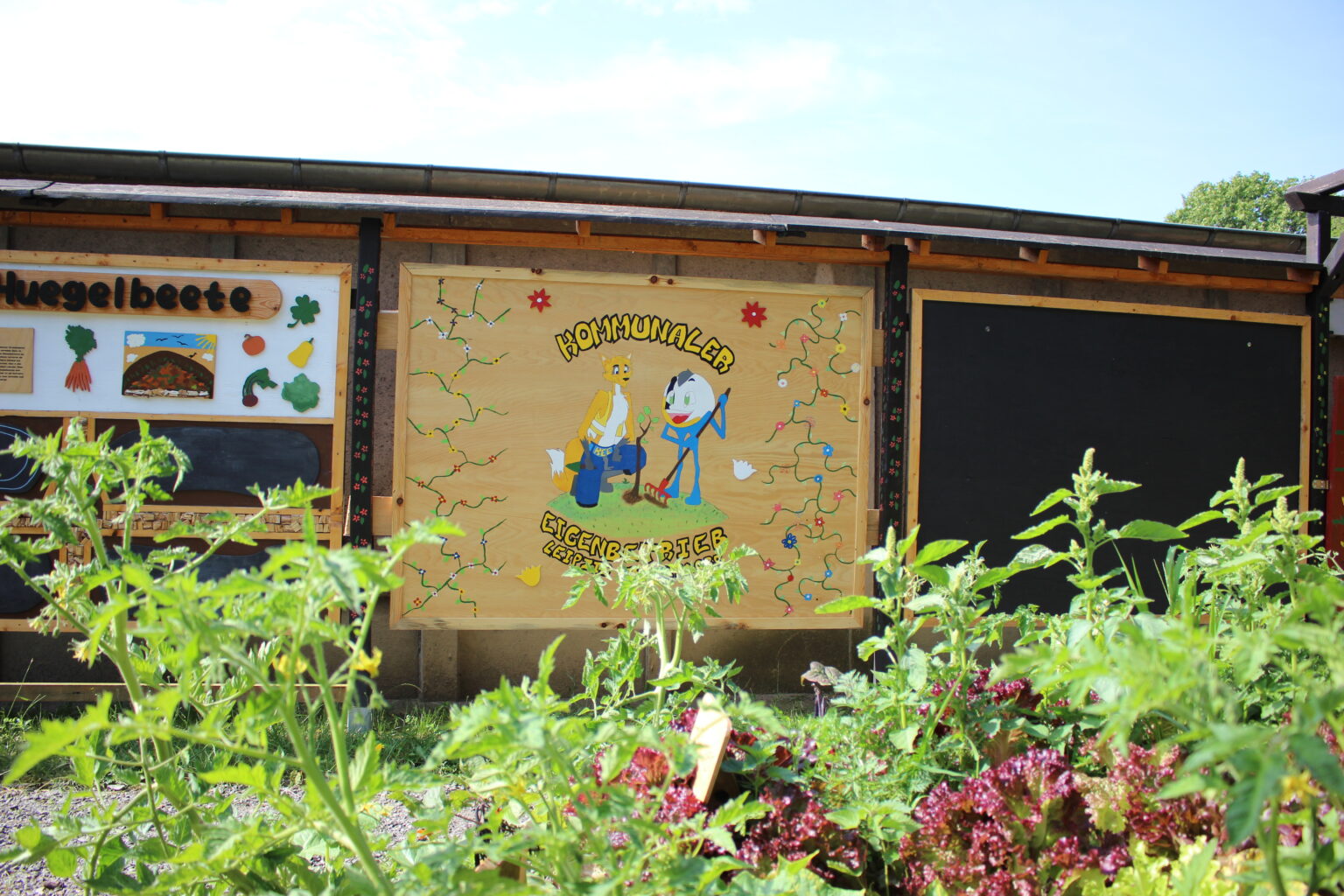 Holztafel mit dem Namen und Maskottchen des KEE. Ein Fuchs und eine Kugelfigur.